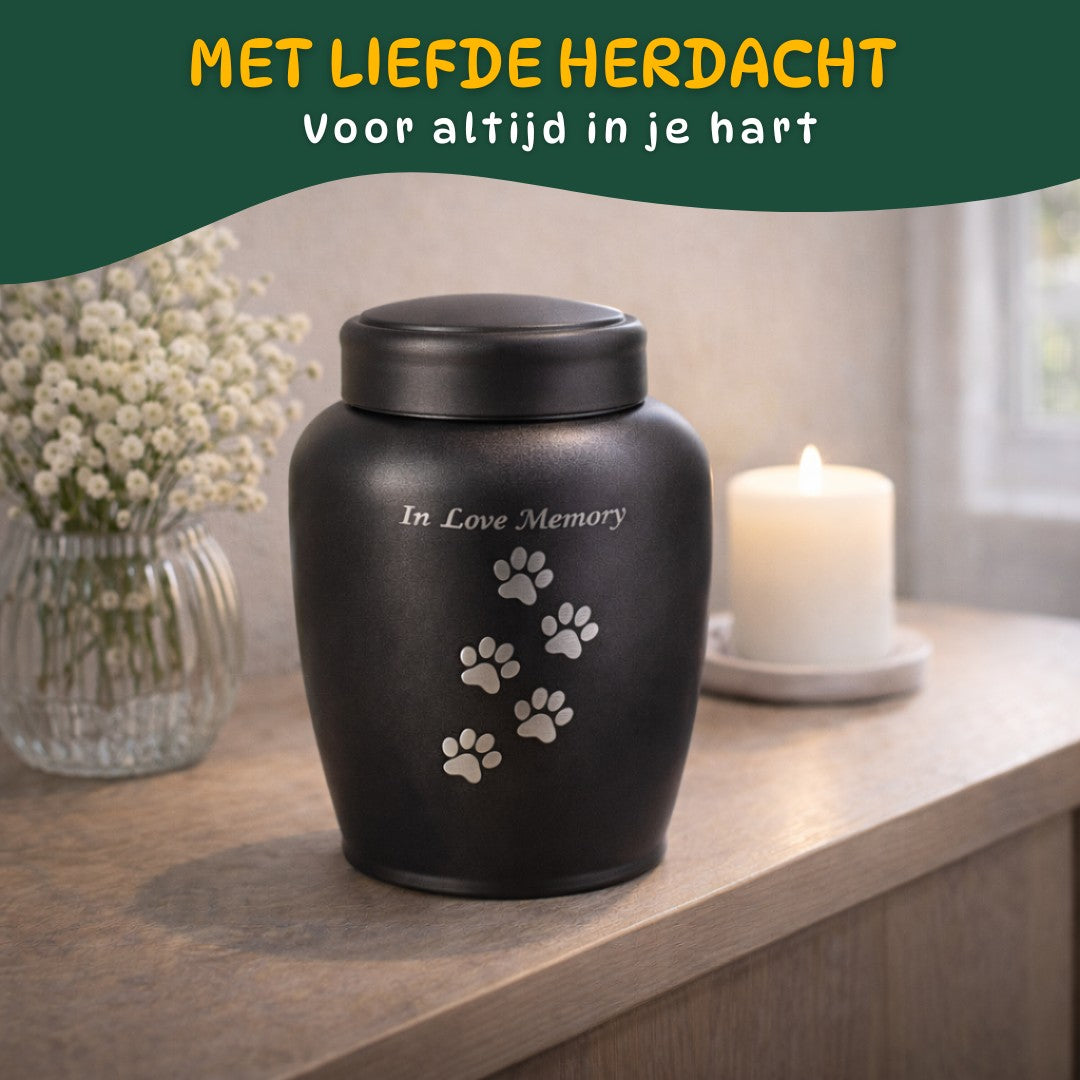 zwarte hondenurn met zilveren pootafdrukken en tekst In Love Memory op houten plank met bloemen en kaars warme herinneringsplek voor hond